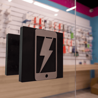 Symbol eines Smartphones mit Blitz an der Tür – Innenansicht des Handy Hero Ladens mit Zubehör an der Wand