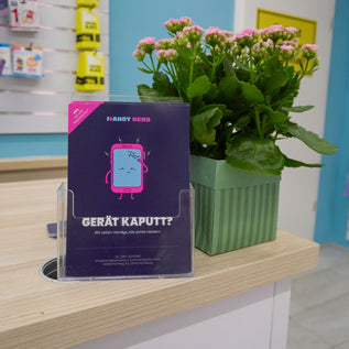 Infokarte von Handy Hero mit Comic-Smartphone und Aufschrift 'Gerät kaputt?' auf der Verkaufstheke